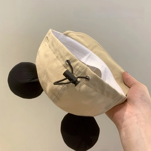 Close-up detail of a beige baby baseball cap featuring black mouse ears and adjustable drawstring
