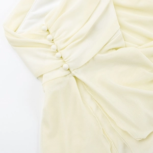 Detail of light yellow slim-fit top featuring delicate pleated fabric and fabric-covered buttons
