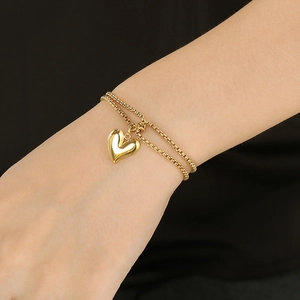 Detail view of a double-layered gold heart pendant bracelet worn on a female wrist