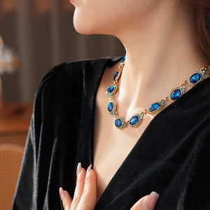 Gros plan d'un collier doré avec gemme bleue ovale sur une tenue en velours noir