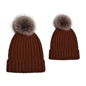 Detail of dark brown knitted beanies with faux fur pom-poms for parent and child matching set