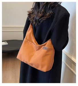 Detail of a large orange nylon hobo bag with side pockets on a model wearing a black coat