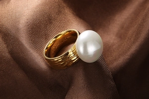 Close-up of a hammered gold steel ring with a large white pearl on brown silk