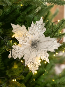 Sparkling white poinsettia ornament with silver sequins on green Christmas tree branch