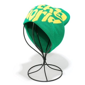 Close-up of green knit beanie featuring yellow jacquard lettering on a metal stand