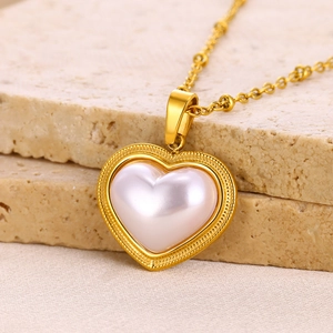 Close-up of gold heart pendant with pearl texture on a beige marble surface