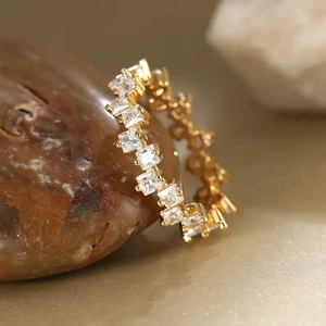 Elegant gold eternity ring with square zircon stones resting on natural brown stone
