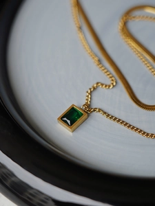 Macro shot of gold emerald zircon layered necklace with snake chain and rectangular pendant