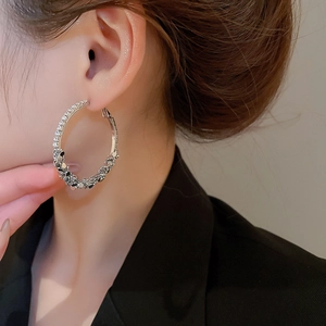 Close-up of silver geometric hoop earrings with shiny pavé rhinestones on a model