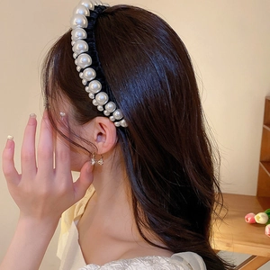 Detail of elegant black velvet headband featuring graduated white pearls on a female model
