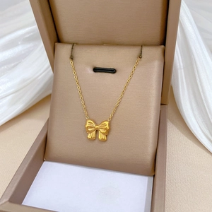 Minimalist gold bow necklace in titanium steel displayed on elegant white silk fabric