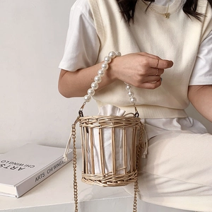 Straw woven bucket bag with pearl handle and chain strap worn by a model in soft lighting
