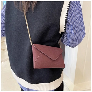Detail of a dark red suede envelope bag with elegant golden chain strap for women