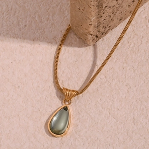 Macro shot of gold-plated snake chain with a teardrop grey stone pendant on a textured stone