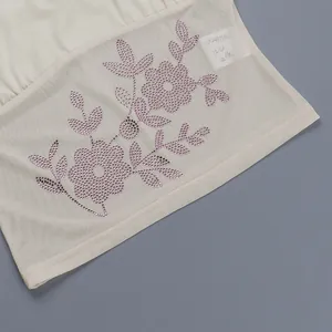 Détail macro du tissu en tulle beige avec motifs de fleurs et feuilles en strass roses