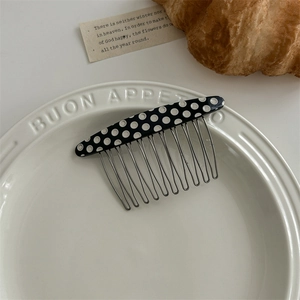 Detail of black hair side comb with white polka dots and silver metal teeth on a plate