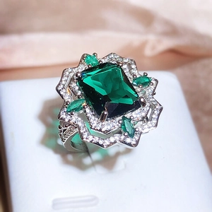 Elegant emerald cut crystal ring with silver flower halo setting on beige fabric
