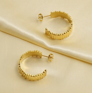 Détail de boucles d'oreilles en C plaquées or 18K avec texture rayée sur satin crème