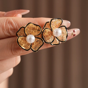 Detailed close-up of woven gold flower earrings with white pearl and black outlines