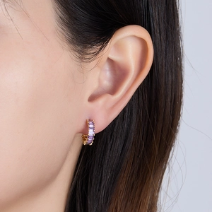 Detail of gold hoop earrings featuring emerald-cut purple zircon stones worn on ear