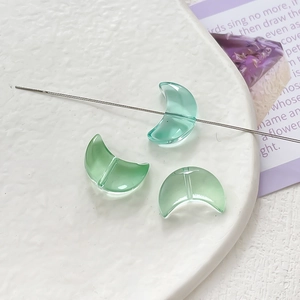 Detailed view of three green crescent glass beads for DIY jewelry making in a white dish