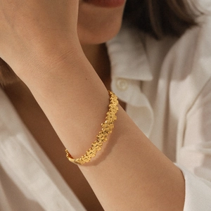 18K gold plated stainless steel daisy floral bangle bracelet worn by model in soft light