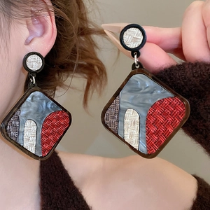 Close-up of geometric diamond earrings with red and grey acrylic marble texture detail