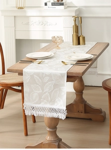 Detailed view of cream jacquard Christmas table runner with leaf patterns and tassels