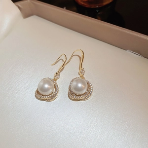 Détail de boucles d'oreilles perles plaquées or avec une auréole de strass brillants