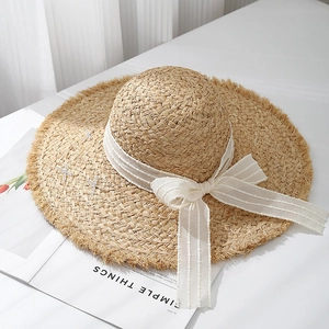 Detail of wide brim raffia sun hat with raw edges and striped bow ribbon decor