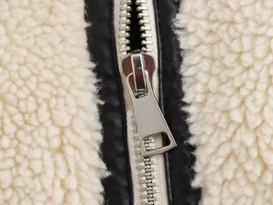 Detailed close-up of silver metal zipper with beige faux shearling and black PU leather trim