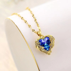Elegante goldene Halskette mit blauem Kristallherz-Anhänger und Flügeln auf weichem Hintergrund