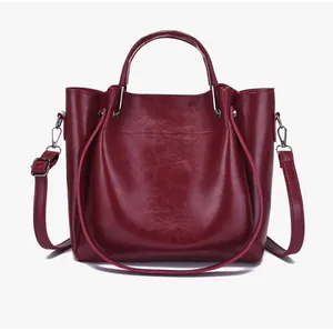 Close-up of glossy wine red handbag featuring round metal handles and adjustable strap