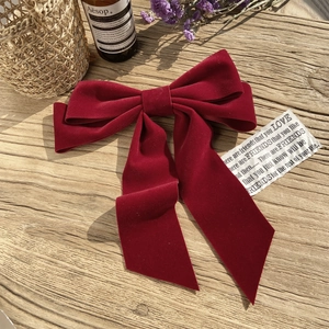 Elegant burgundy velvet bridal bow hair clip with long ribbons on a rustic wood surface