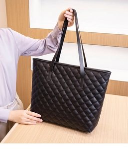Detail of black quilted tote bag with diamond pattern stitching and dual shoulder straps