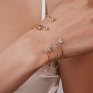 Détail de bracelets ouverts dorés avec zircons en forme de cœur, d'étoile et de goutte au poignet