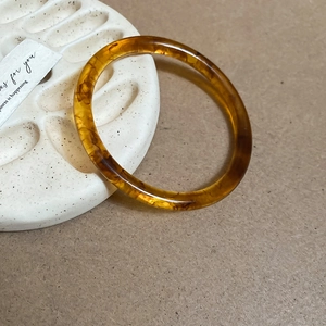 Detailed view of amber resin bangle showing translucent tortoiseshell texture on ceramic stand