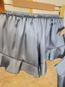 Detail of silver satin sleep shorts featuring elastic waistband and delicate ruffle hem