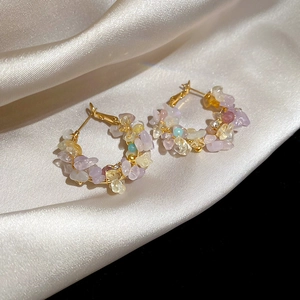 Close-up of golden hoop earrings with colorful irregular natural stones on silk fabric