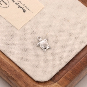 Macro detail of a polished stainless steel sea turtle pendant on a rustic linen background