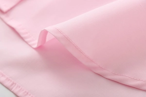 Detail of pink cotton shirt hem showing precise single-needle stitching on plain fabric