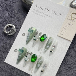 Close-up of long stiletto press-on nails with green cat-eye, pearls, and metal chains