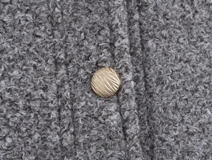 Gros plan sur un bouton doré sur tissu sherpa gris montrant les détails d'un vêtement chic