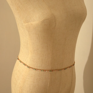 Detail of bohemian gold body chain with colorful teardrop pendants on a beige mannequin
