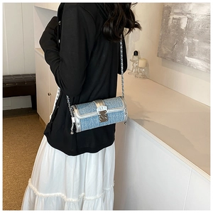 Detail of blue denim cylinder crossbody bag with silver chain strap and metal rivet trim