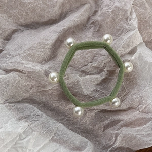 Detail of green elastic hair tie with pearl accents and knit texture on beige paper