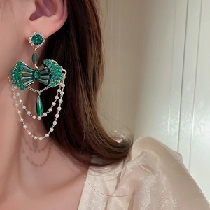 Detail of green crystal bow earrings with elegant pearl tassel chains on model