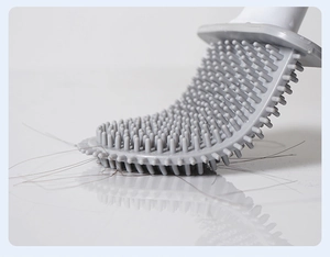 Close-up of gray silicone toilet brush head bending to clean hair on smooth surface