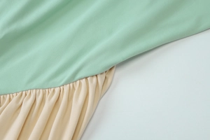 Detailed close-up of light green and beige patchwork fabric with pleated texture on dress