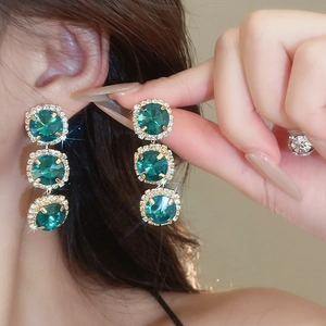 Detail of elegant gold earrings with three green gemstones and diamond-like rhinestones